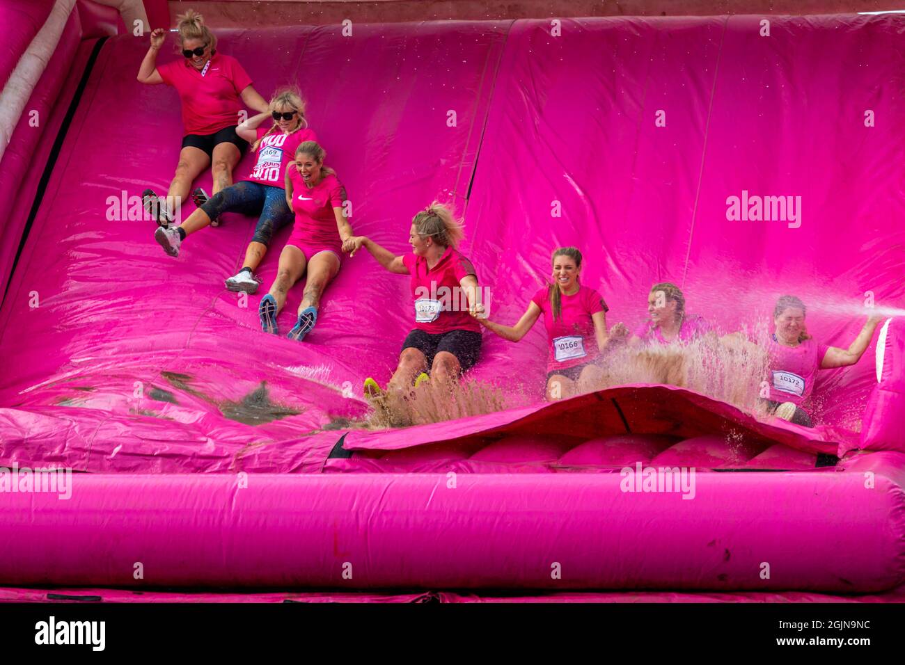 Baiter Park, Poole, Dorset, UK. 11th September 2021. Race for Life Poole Pretty Muddy returns after being cancelled last year due to Covid-19, with hundreds many dressed in pink, joining the fight to beat cancer and raise money for Cancer Research UK, negotiating obstacles throughout the 5km course and have fun getting covered in mud. Having fun on the inflatable slide. Credit: Carolyn Jenkins/Alamy Live News Stock Photo