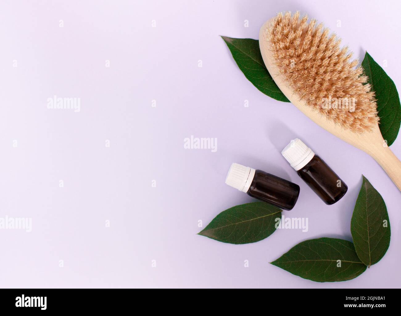 wooden brush for anti-cellulite body massage, and cosmetic bottle on purple light background. Body care concept Stock Photo