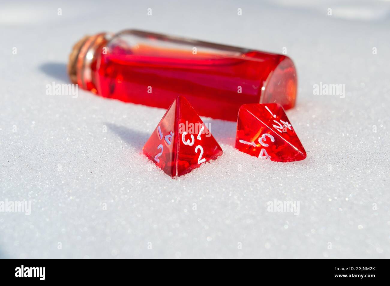Close-up image of two red 4-sided role-playing game dice in the snow. In the background a glass stopper bottle  with red liquid Stock Photo