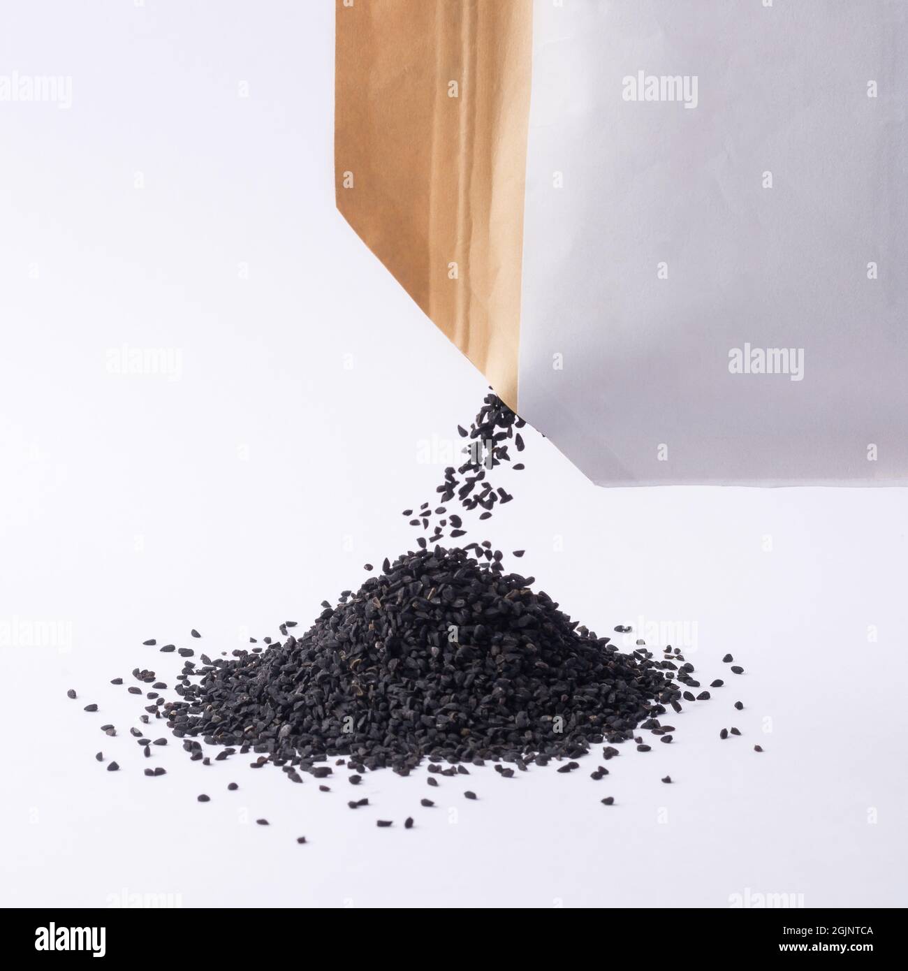 heap of black seeds, also known as black cumin or caraway or kalonji, poured out from a packet, mockup template, isolated on neutral background, close Stock Photo