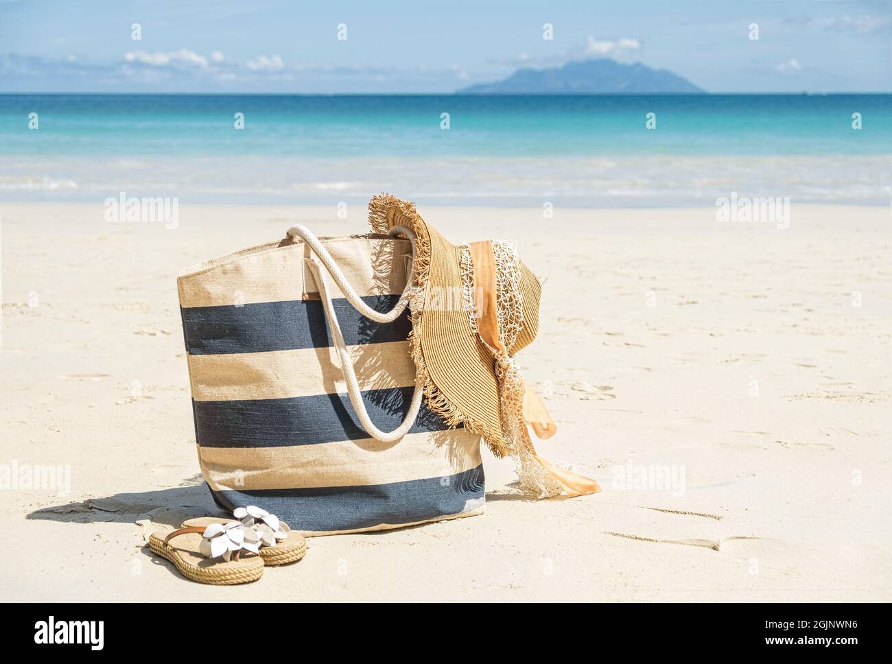 Blue and beige stripy beach bag, straw hat and flip flops on tropical