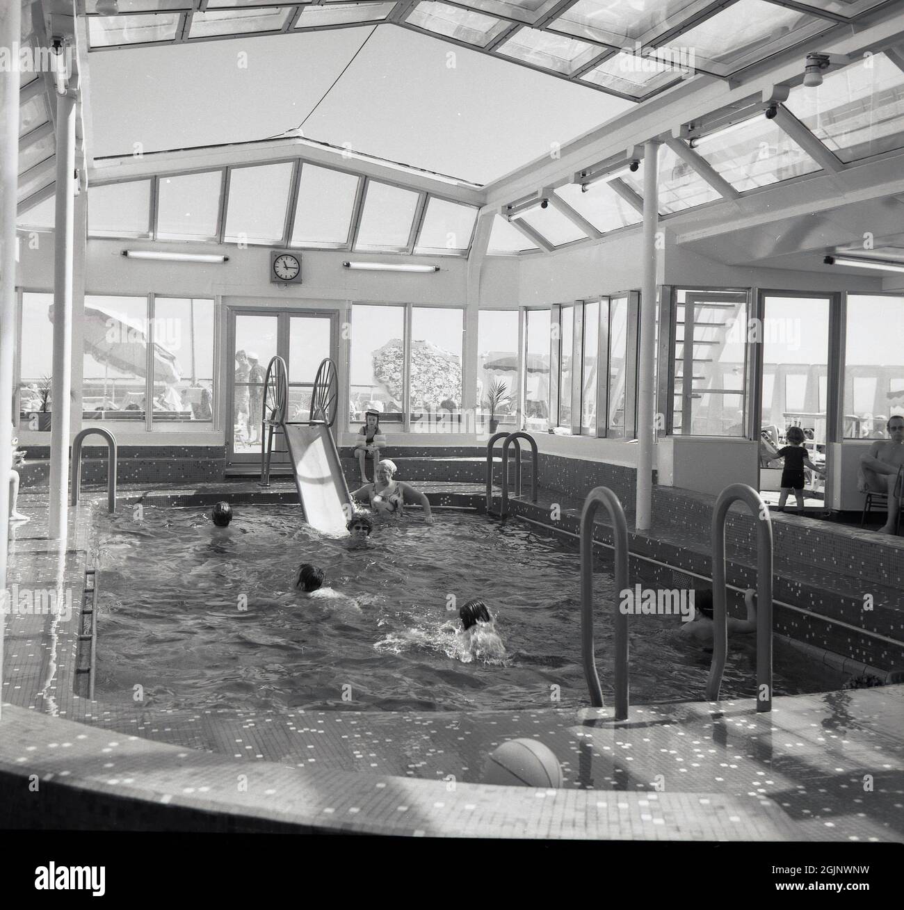 1965, historical, cruise ship passengers enjoying the covered swimming pool on the Sagafjord ocean liner. Built for the Norweigian America Line and one of the most luxuriors liners of her day, the construction of the cruise ship was so expensive that it put the shipyard that built it, the long-established French FCM company, out of business. Her maiden voyage was from Oslo to New York in October 1965 and she set a new benchmark for luxury at sea. The ship was voted amongst the 10 best cruise ships in the world until the early 1990s. Stock Photo