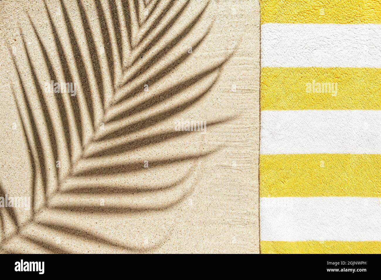 Stripy yellow and white beach towel and palm leaf shadow on sandy beach
