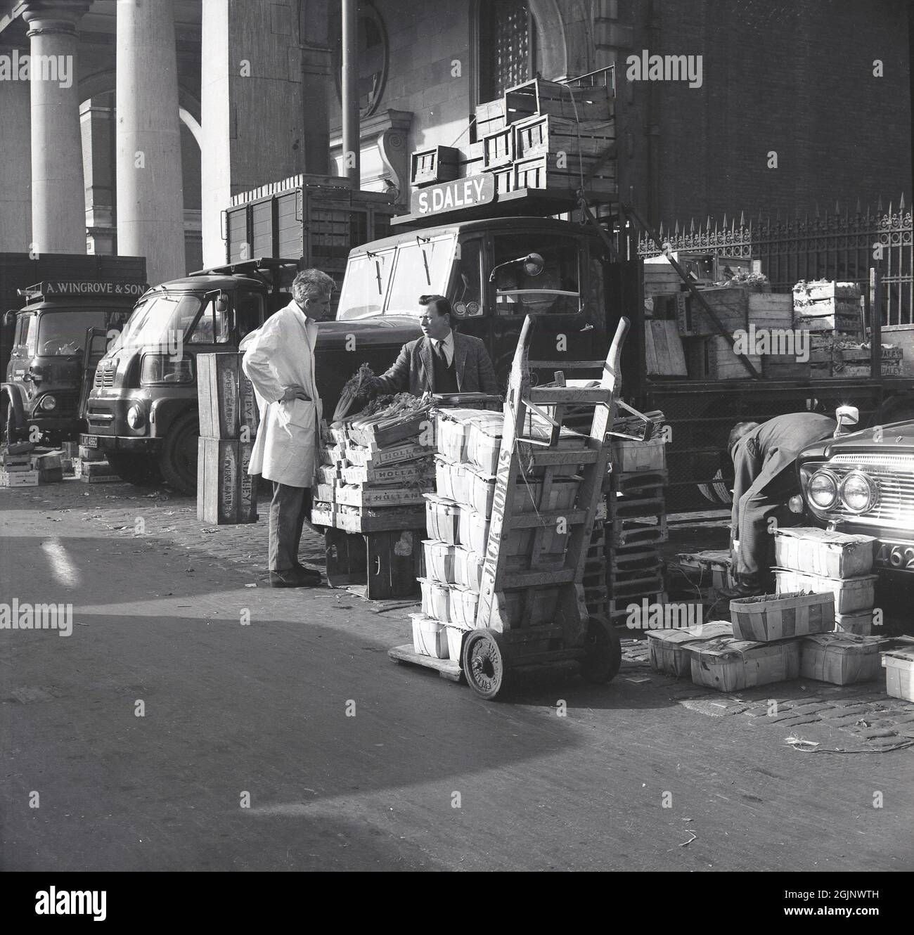 1950s, historical, in the delivery area of the old Covent Garden fruit, vegetable and flower market, in central London, England, UK, a market trader talking to a porter, as crates of vegetables, including celery from Holland, are being unloaded from a truck at the market pitch of S. Daley. The size of the market was such that at its height, it would receive almost a third of all the fruit and vegetables imported into the country. Due to size in a small part of the city, in 1974 the market was relocated. Stock Photo