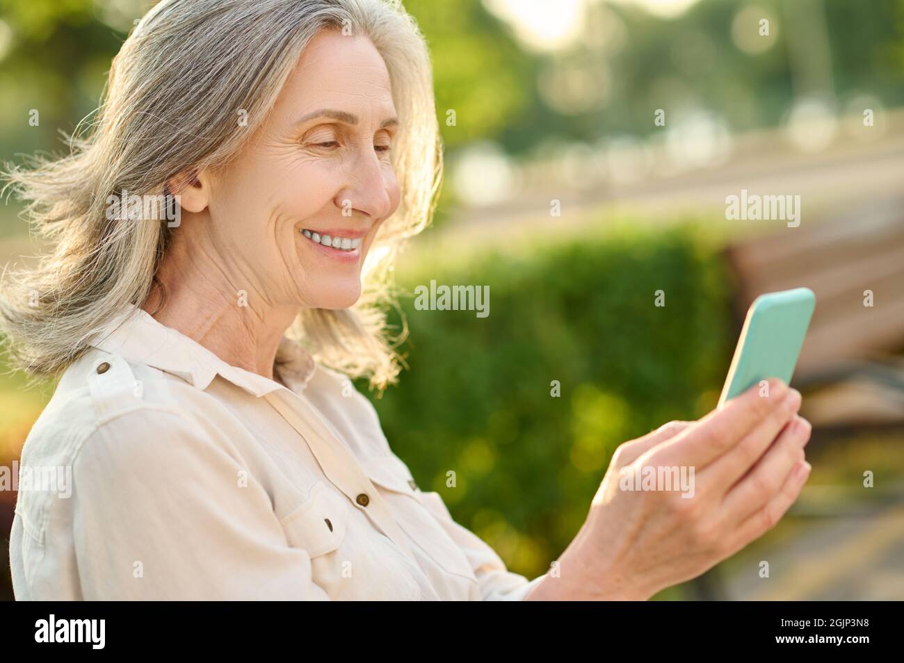 Smiling adult woman with smartphone in park Stock Photo