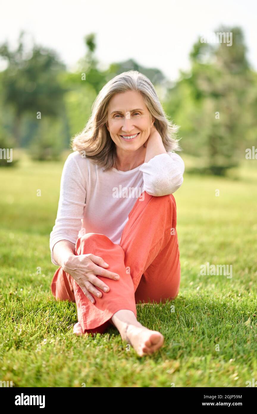 Smiling woman barefoot sitting on grass Stock Photo
