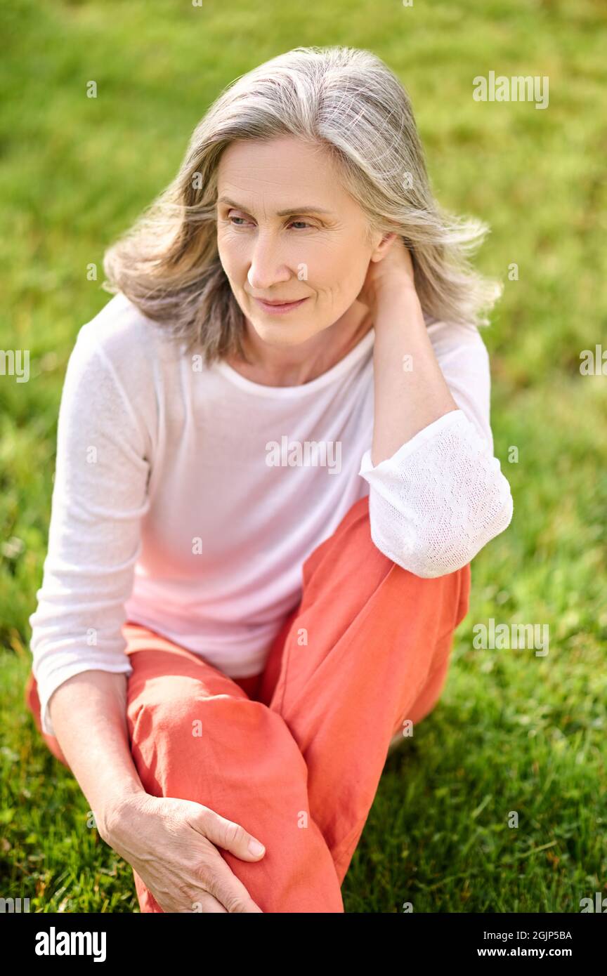 Gray-haired woman meditating on green lawn Stock Photo
