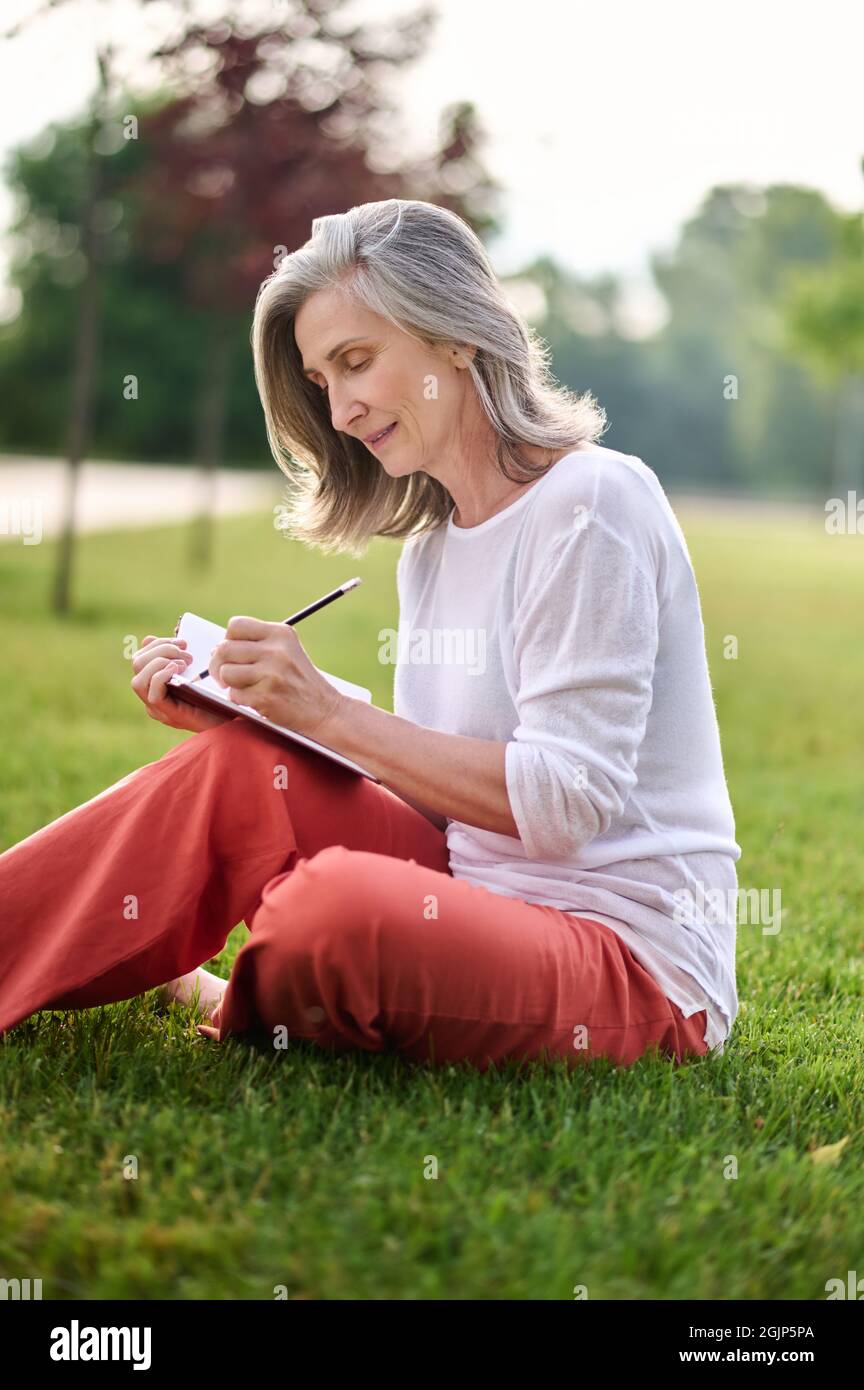 Woman writing in notebook on grass in park Stock Photo