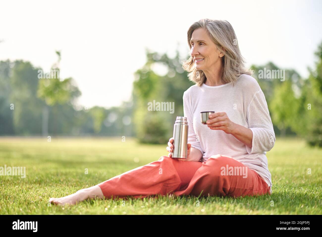 Woman with thermos sitting on grass in park Stock Photo