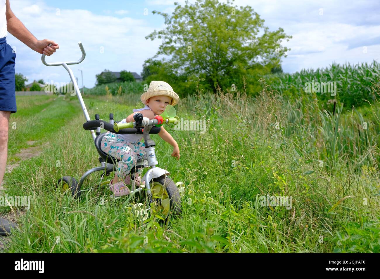 portrait of a cute little girl in a hat sitting on a small bicycle on a dirt road Stock Photo