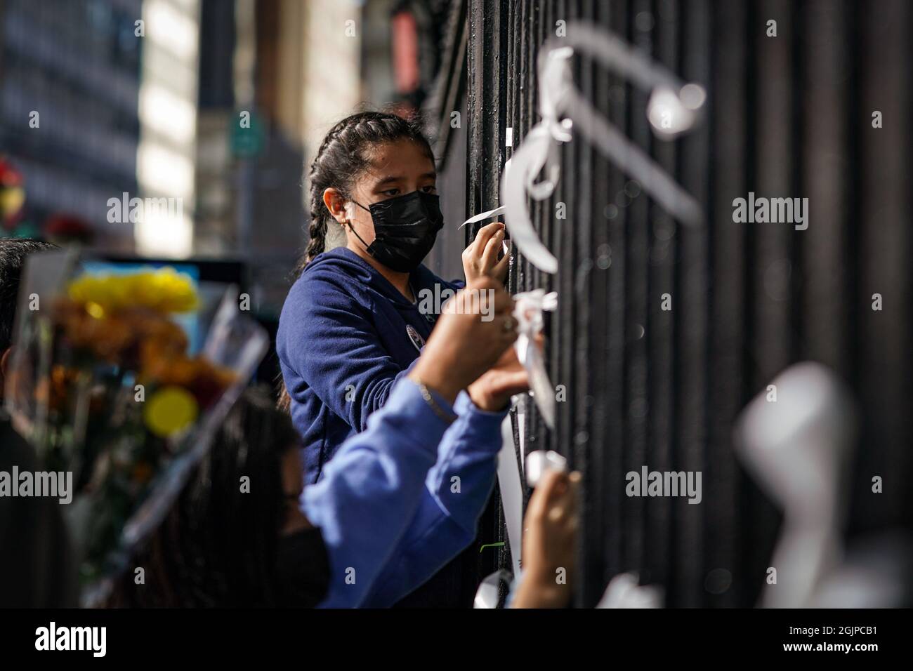 New York, USA. 11th Sep, 2021. A girl ties a white ribbon to the fence of St. John’s Chapel in front of One World Trade Center on the 20th anniversary of the September 11th terrorist attacks in New York, USA. Credit: Chase Sutton/Alamy Live News Stock Photo
