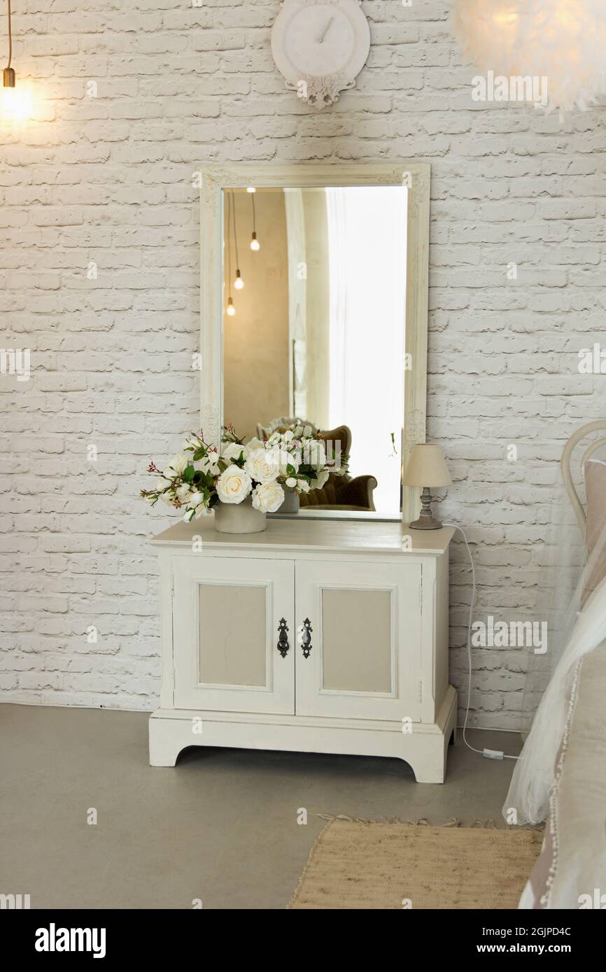 White elegant bedside table with square mirror located in bedroom as interior cosy room Stock Photo