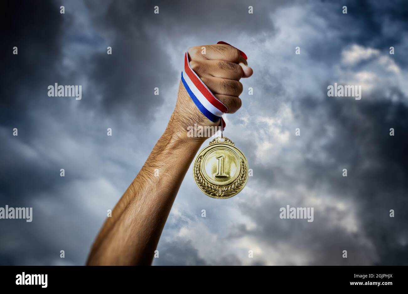 Medal for first place in the athlete hand against a dramatic sky. Winner gold award. Sport champion victory and success concept Stock Photo