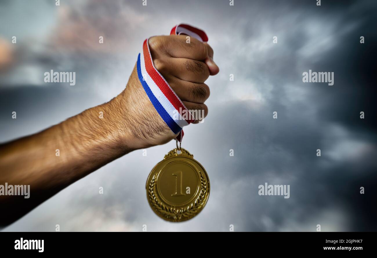 Hand holding gold medal against cloudy twilight sky background, in hand. First place award on cloudy sky background, Sport champion winner athlete and Stock Photo