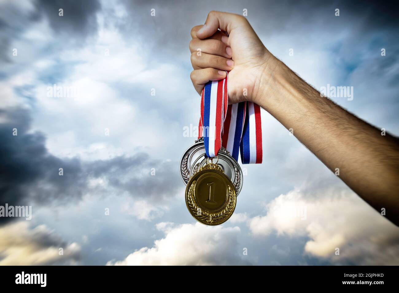 Medals in the athlete hand against a dramatic sky. Winner award, gold silver and bronze. Sport champion victory and success concept Stock Photo