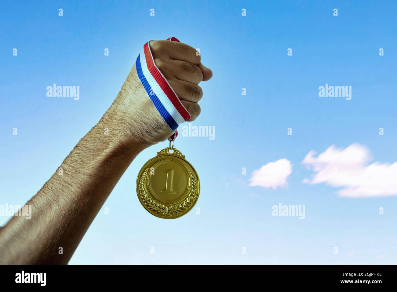 Medal gold in winner hand. First place award on clear blue sky background, Sport champion athlete victory concept Stock Photo