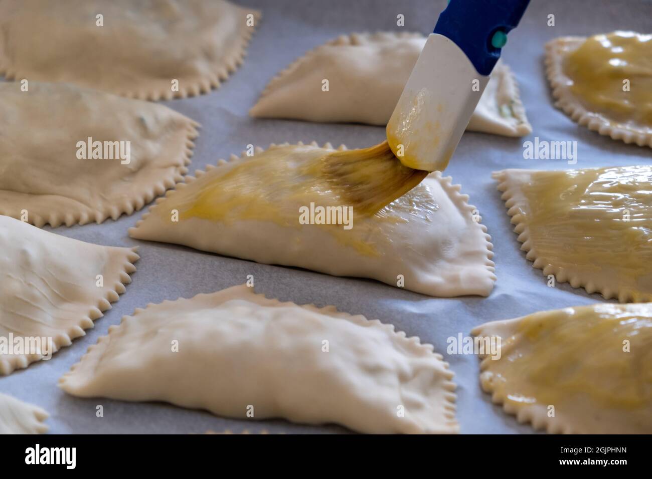 Kalitsounia traditional healthy Cretan food, Greece. Above close up view of kaltsounia uncooked pies some smeared with egg on non stick paper for baki Stock Photo