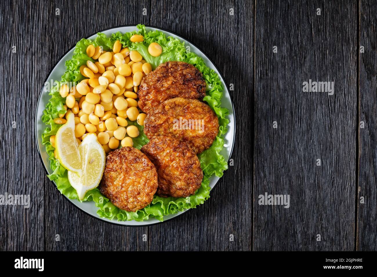 baked pork patties with browned cheese crust on a green lettuce lives with lupin beans and lemon, flat lay, free space Stock Photo