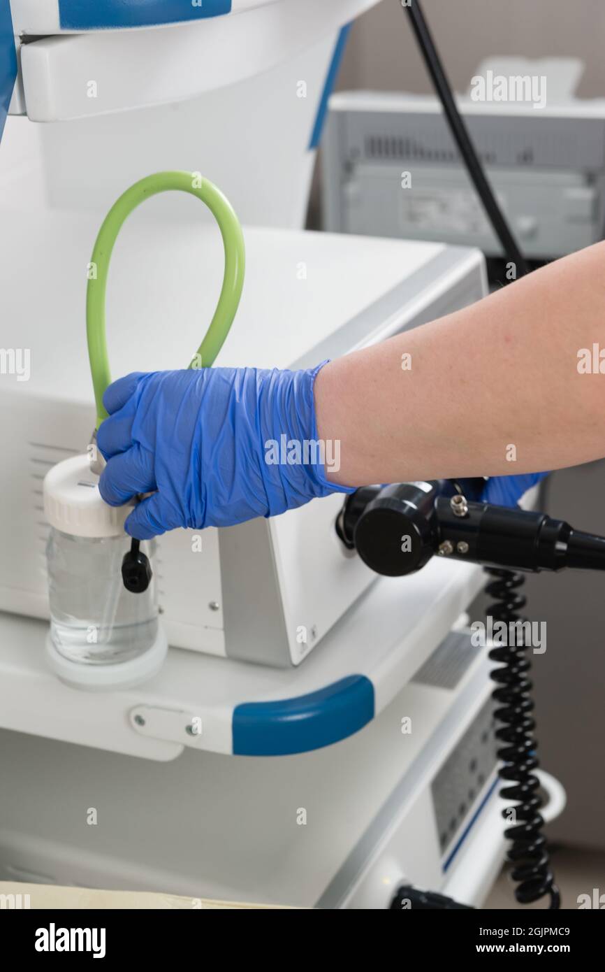 Preparation of equipment for the medical examination of gastroscopy. A hand in a blue glove connects an endoscope and a container of water Stock Photo