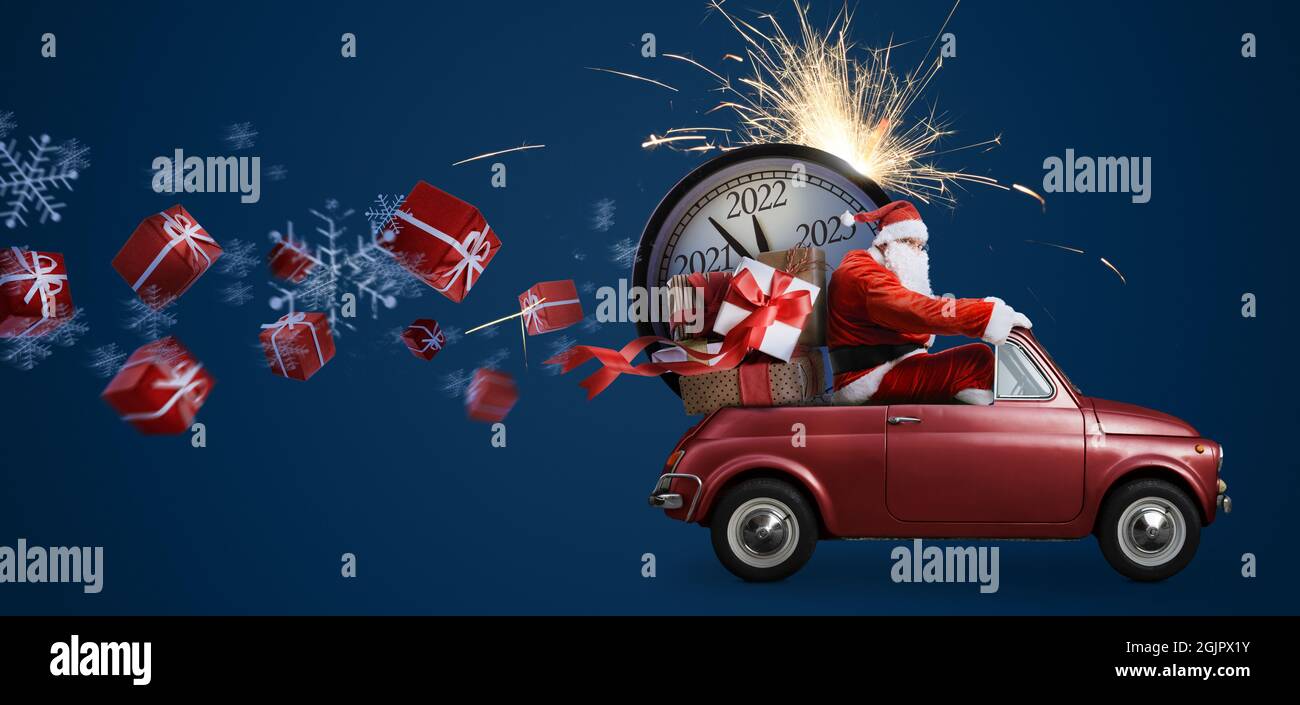 Christmas is coming. Santa Claus on toy car delivering New Year 2022 gifts and countdown clock at blue background with fireworks Stock Photo