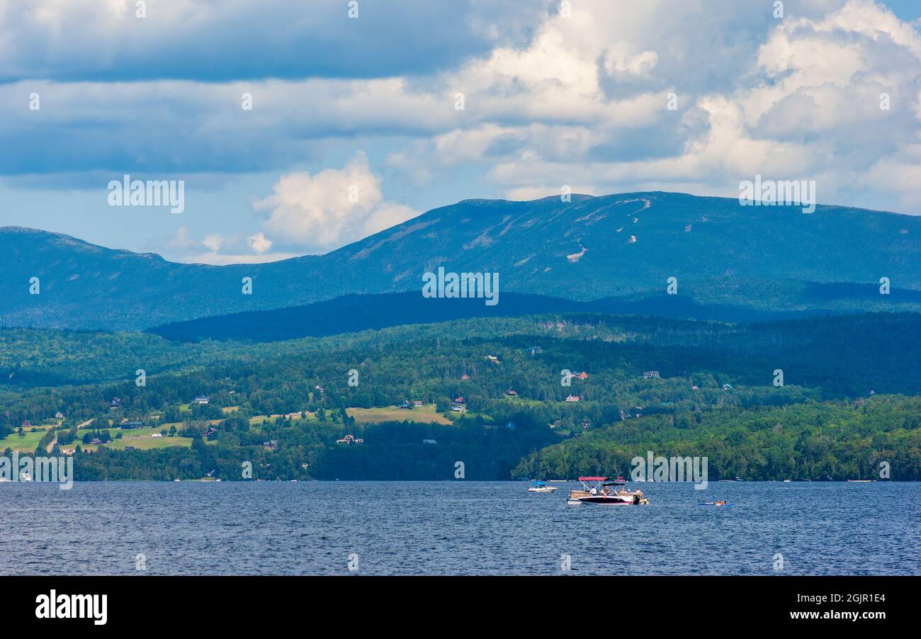 Recreational boats on Rangeley Lake, in Maine. Town of Rangeley on the shoreline, up the hill. Saddleback Mountain on the back, under a cloudy sky. Stock Photo