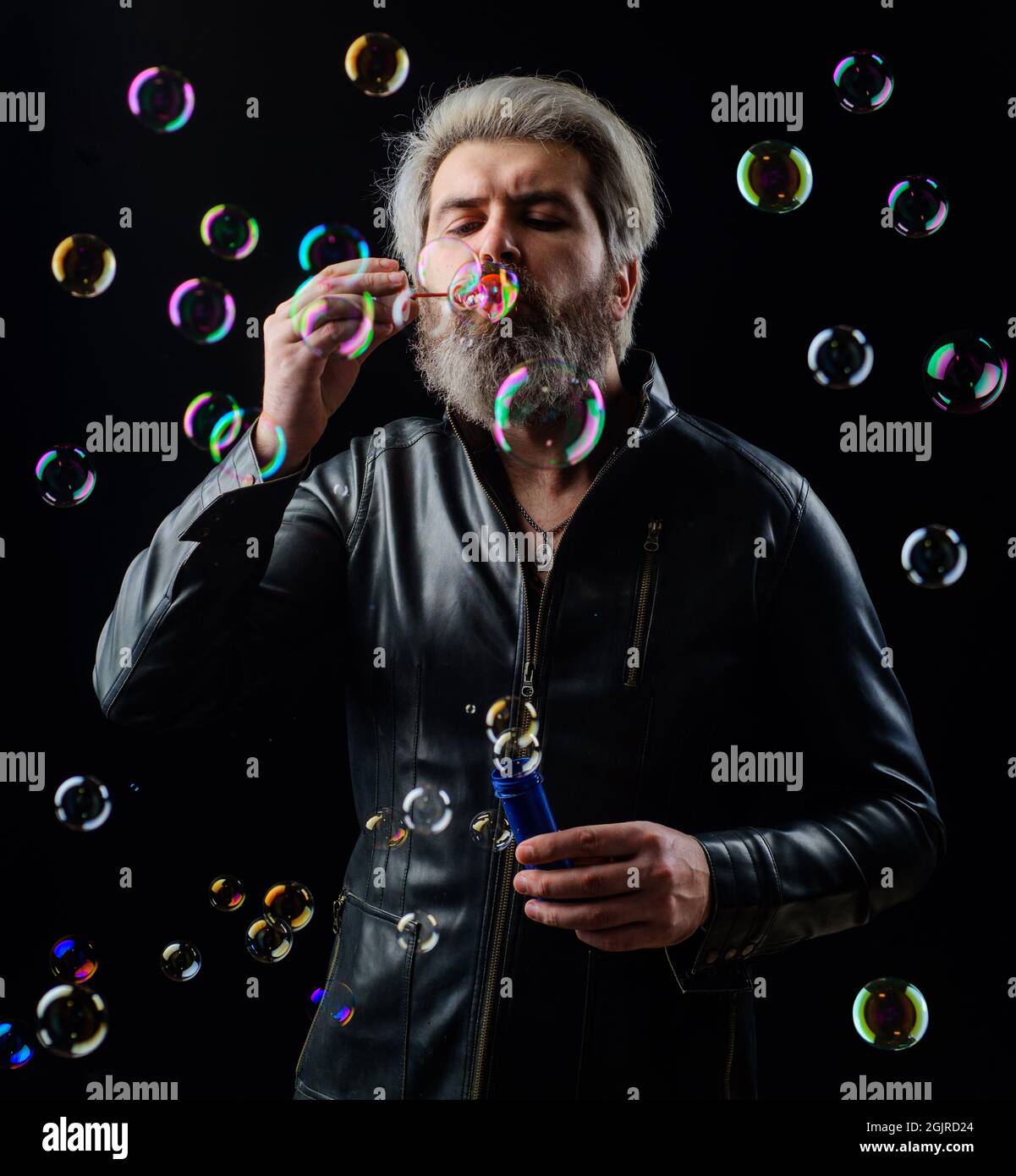 Man in leather jacket blowing Soap bubbles. Happiness. Good mood. Childhood concept. Bearded guy Plays with bubbles. Stock Photo