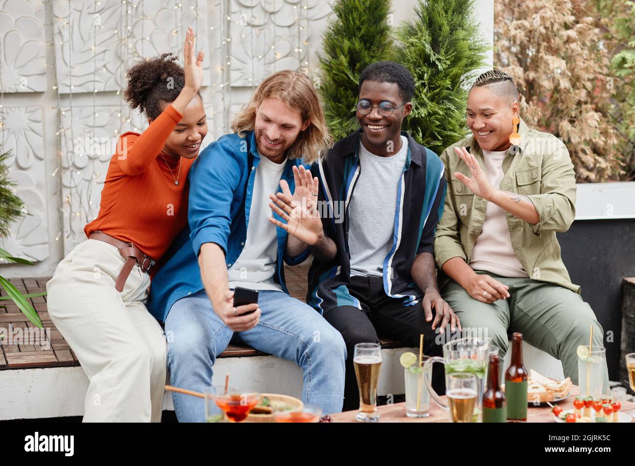 Diverse group of young people waving at camera via video chat while having  fun during outdoor party at rooftop Stock Photo - Alamy