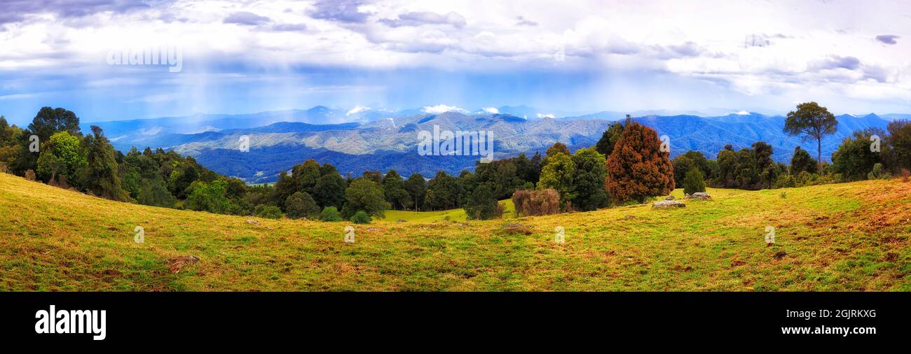 Cultivated grazing farm high in Dorrigo of Australia - scenic landscape with distant storm and rain over mountains. Stock Photo