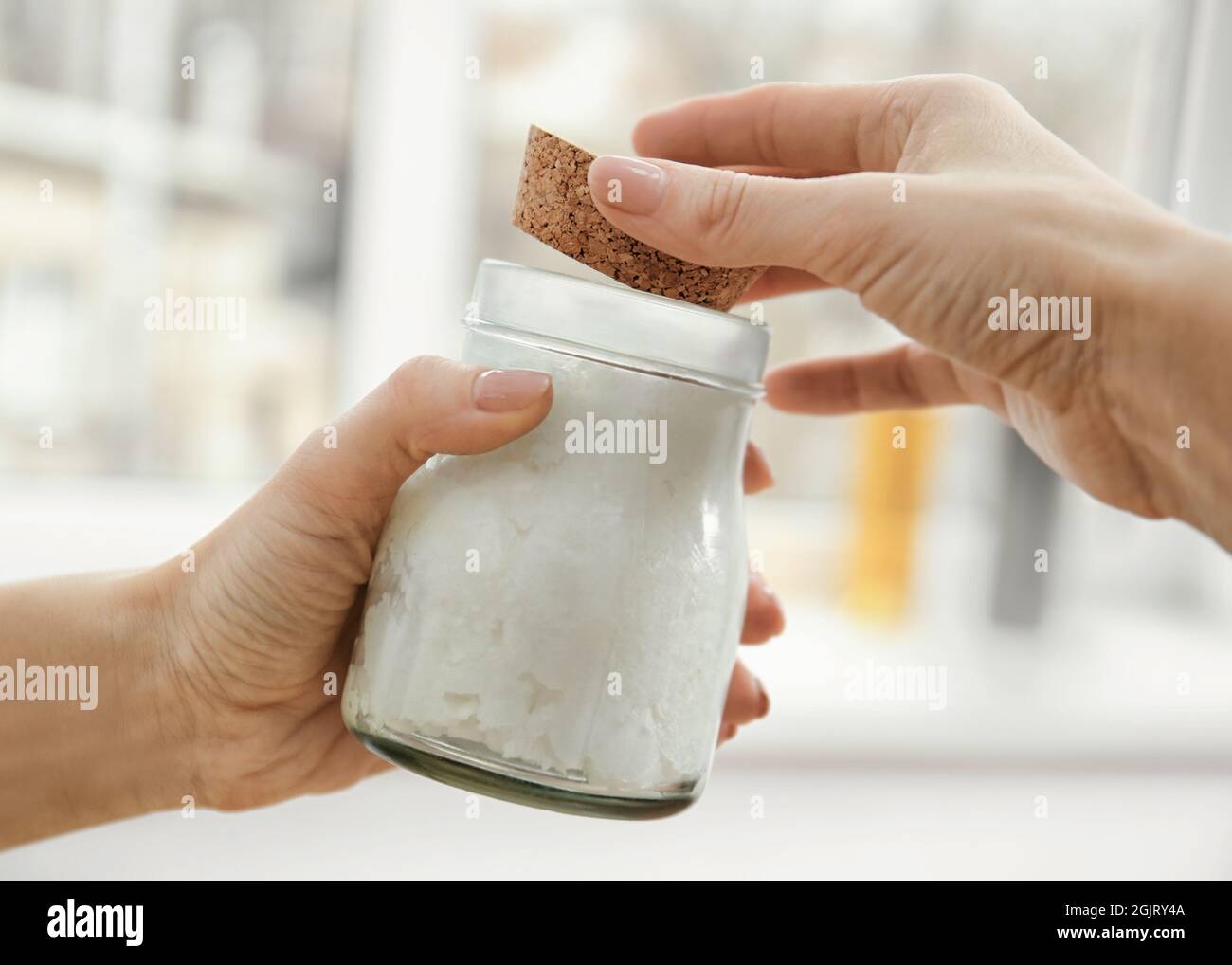 Female hands holding jar with coconut oil on blurred background Stock