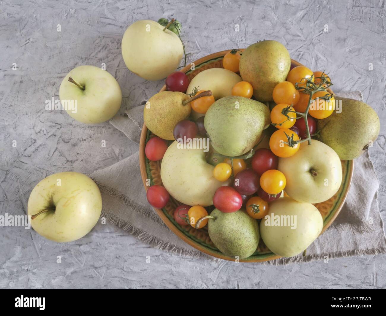 Ripe apples, pears and plums are on the table in a ceramic plate Stock Photo