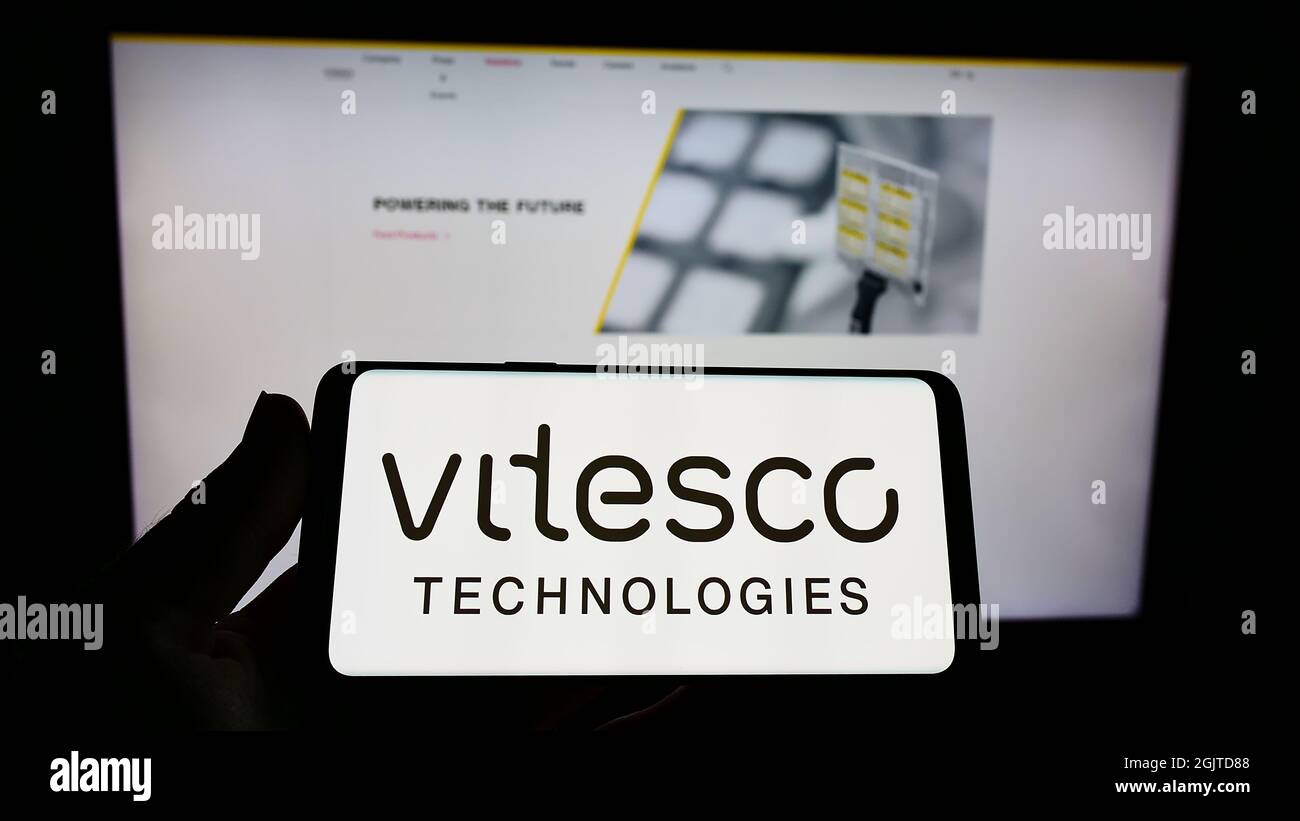 Person holding cellphone with logo of German automotive supplier Vitesco Technologies on screen in front of webpage. Focus on phone display. Stock Photo
