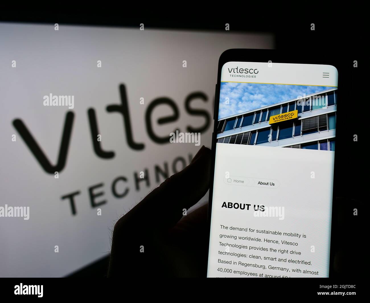 Person holding smartphone with webpage of German automotive supplier Vitesco Technologies on screen with logo. Focus on center of phone display. Stock Photo