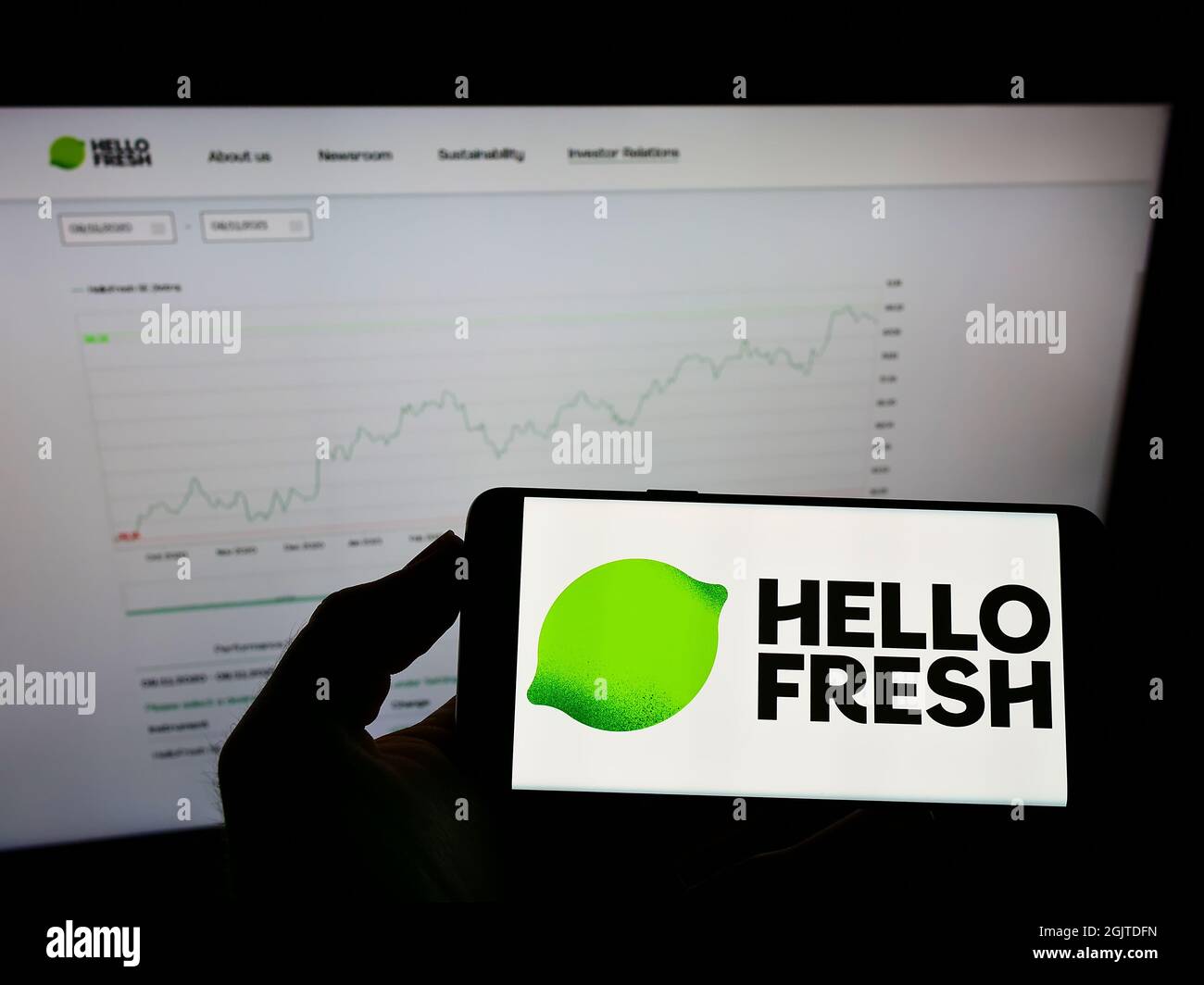 Person holding mobile phone with logo of German meal-kit company HelloFresh SE on screen in front of business web page. Focus on phone display. Stock Photo