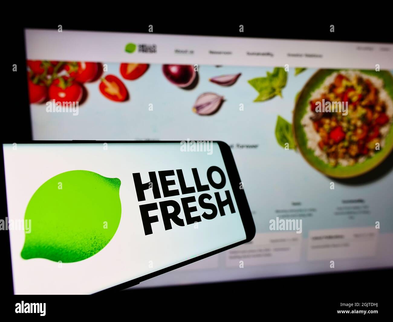 Cellphone with logo of German meal-kit company HelloFresh SE on screen in front of business website. Focus on center-right of phone display. Stock Photo