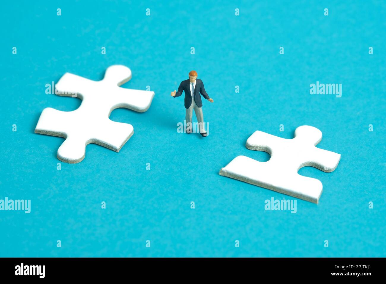 Miniature people toy figure photography. A shrugging businessman standing the middle of two puzzle jigsaw piece. Isolated on blue background. Image ph Stock Photo