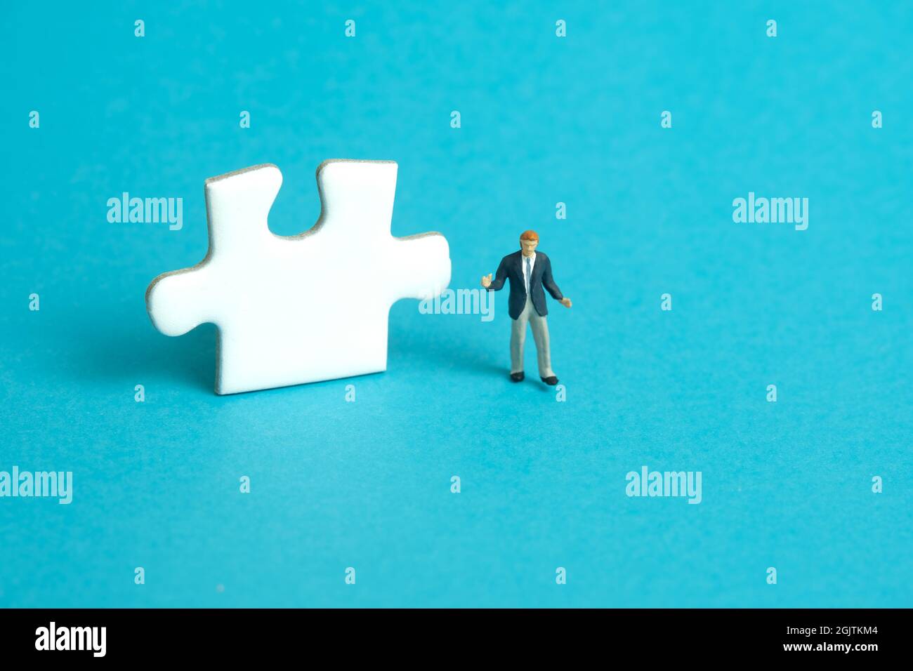 Miniature people toy figure photography. A shrugging businessman standing in front of puzzle jigsaw piece. Isolated on blue background. Image photo Stock Photo