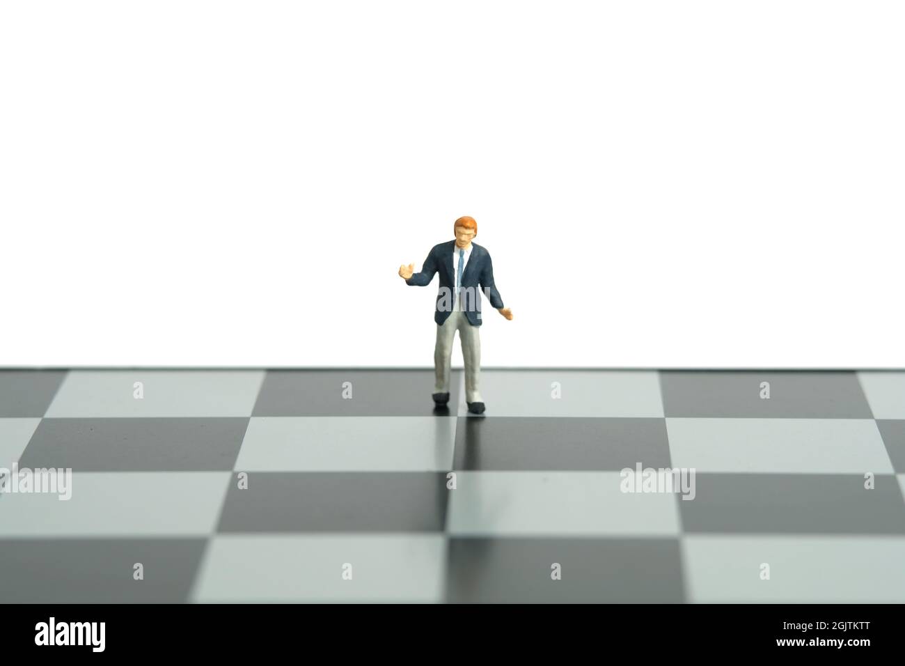 Miniature people toy figure photography. Strategy decision concept. A shrugging unsure businessman stand above chessboard. Isolated on white backgroun Stock Photo