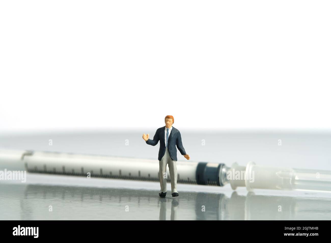 Miniature people toy figure photography. Hesitation on vaccination concept. A shrugging businessman standing in front of syringe vaccine. Isolated on Stock Photo