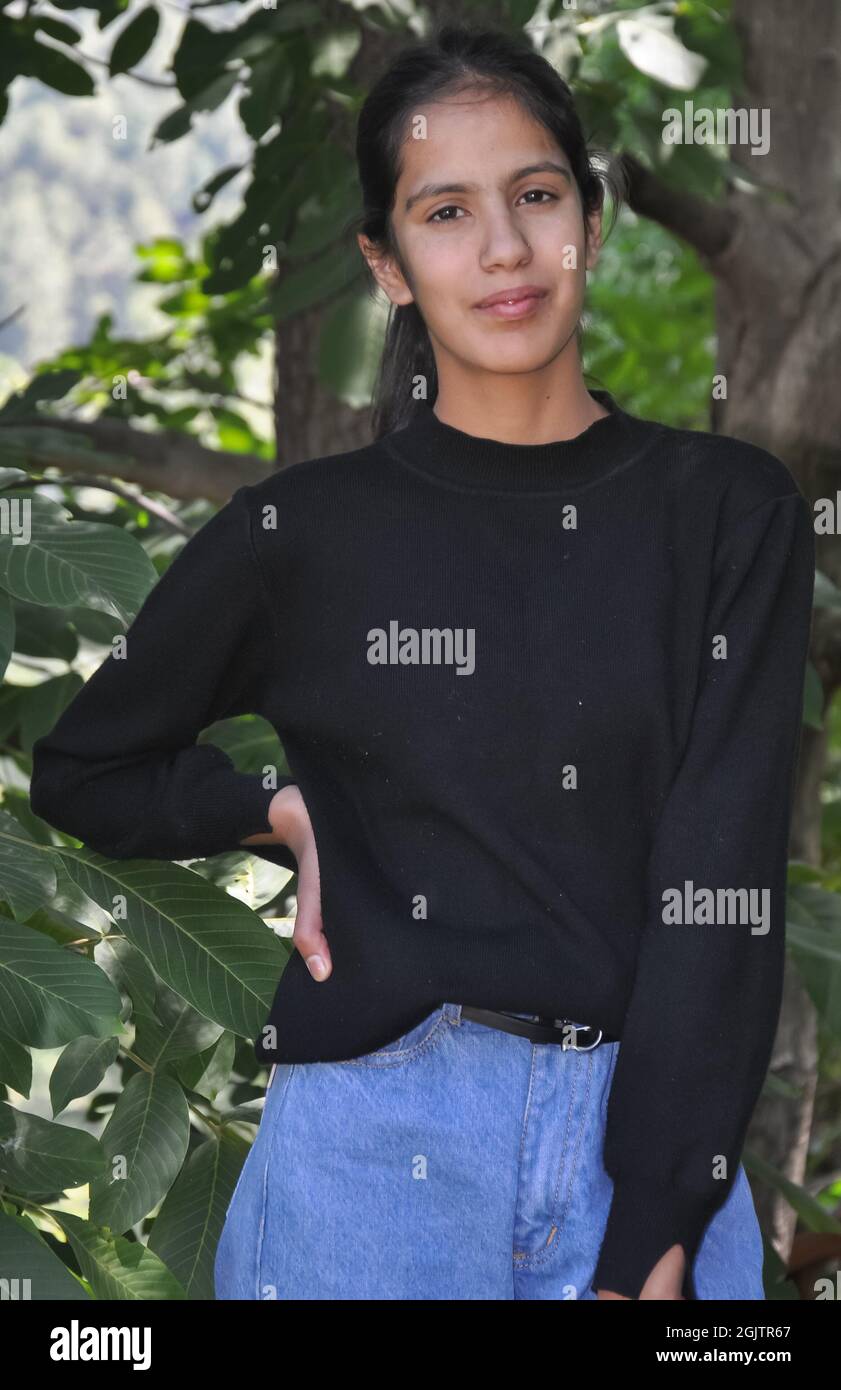 Portrait of a charming young girl standing outside and wearing black sweatshirt and light blue jean and posing with her hand on hips and looking at camera Stock Photo