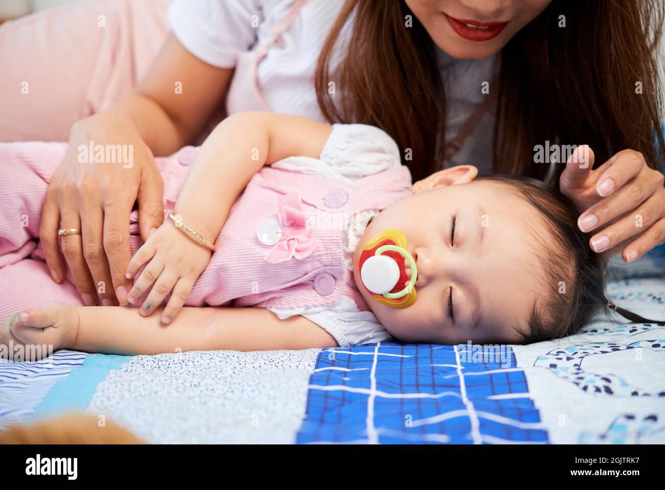 Young mother looking at baby girl with pacifier in mouth sleeping on