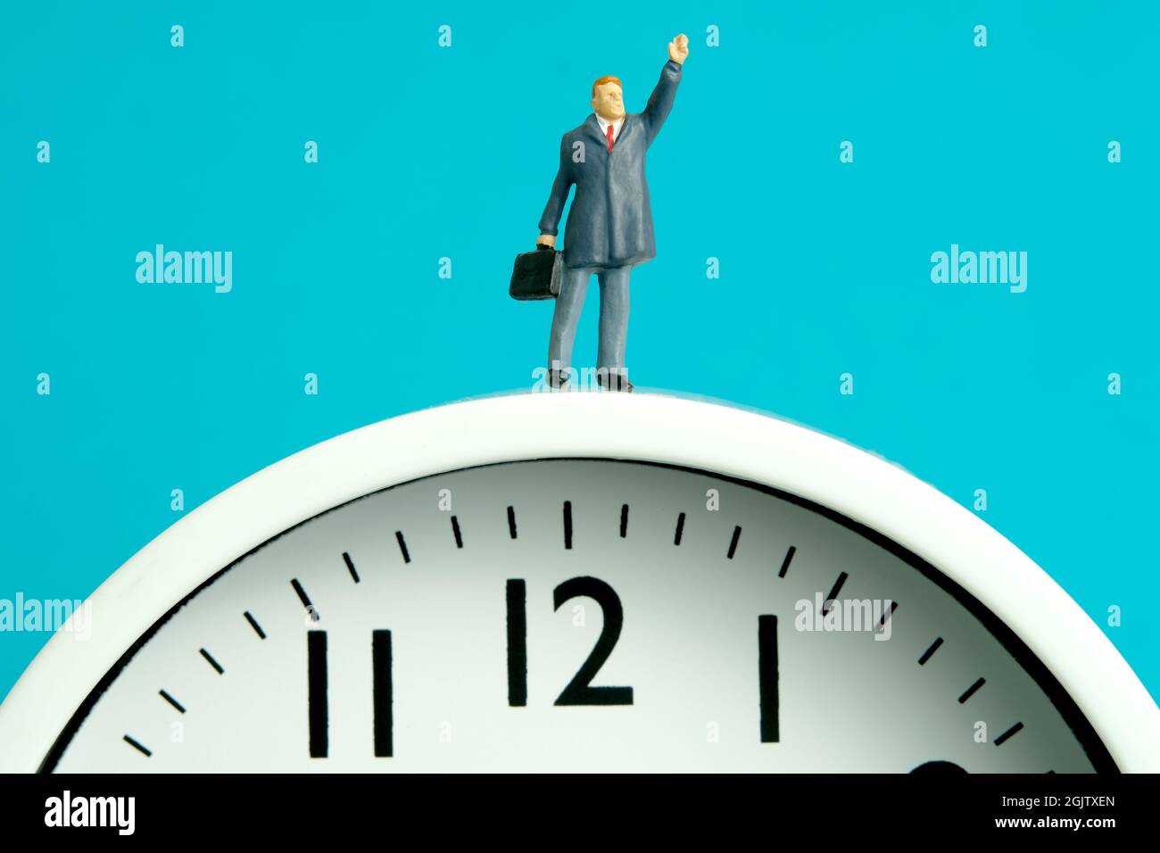 Miniature people toy figure photography. Time management power concept. A businessman standing above clock while raise his hand. Isolated on blue back Stock Photo