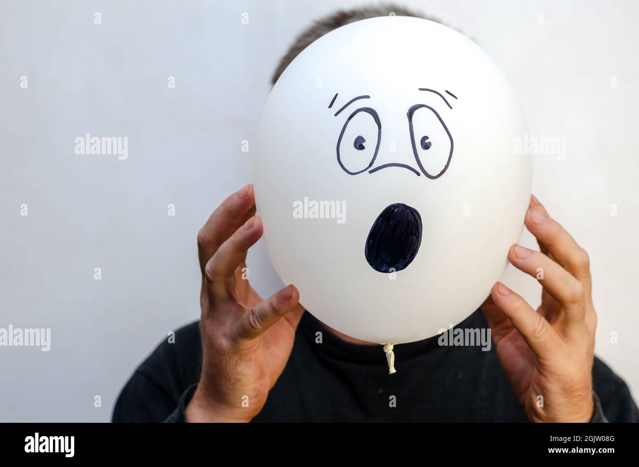 A man is holding a balloon with his face painted on it. The ball Stock