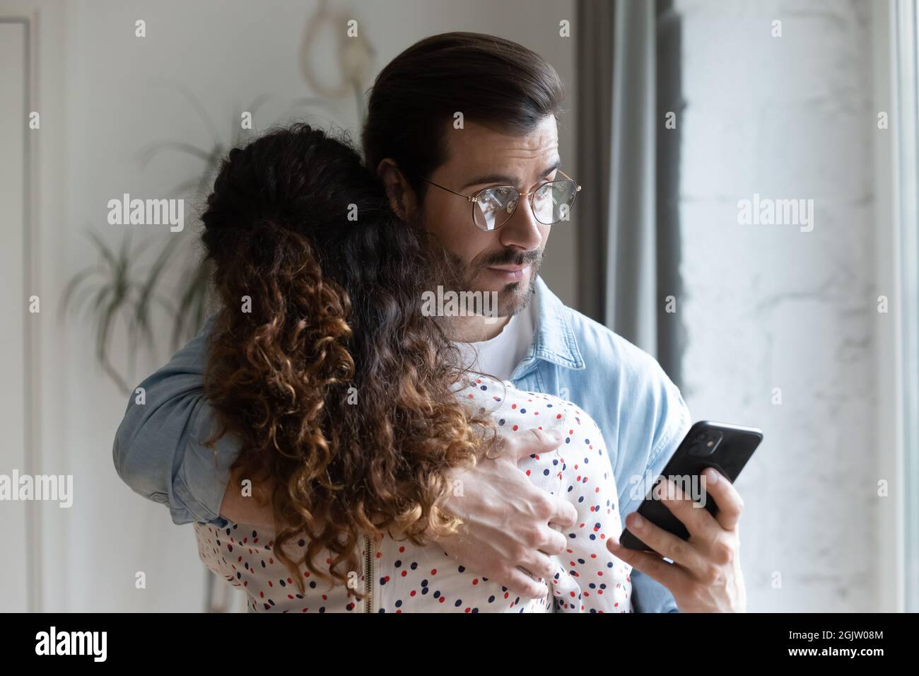 Jealous husband hugging wife and checking her phone Stock Photo