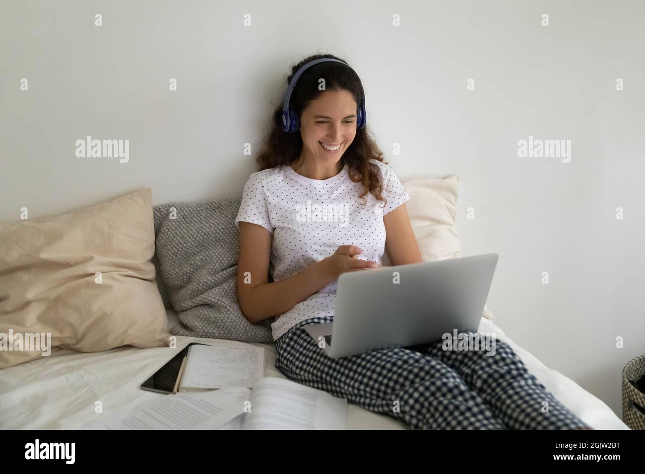 Woman sit in bed wear headphones talking remotely through