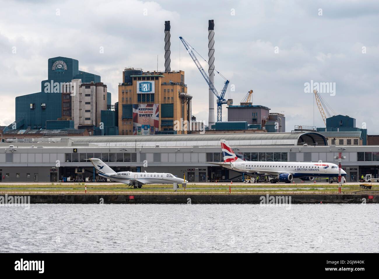 London City Airport, with a British Airways airliner plane, and a business jet on the runway. Private, corporate jet of Mjair Management AB arrival. Stock Photo
