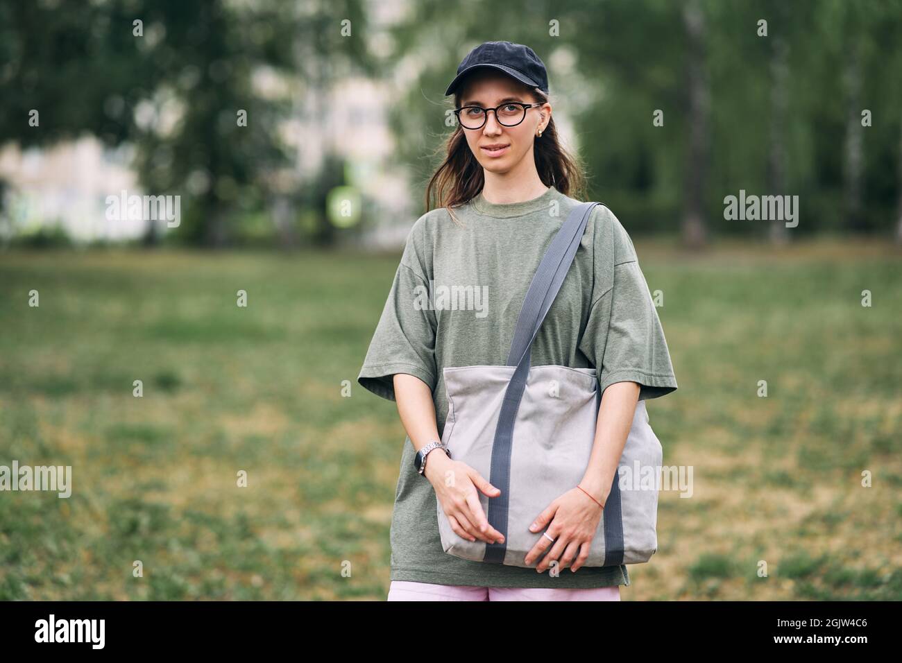 Young woman with glasses holding empty cotton eco bag, mockup design. Stock Photo