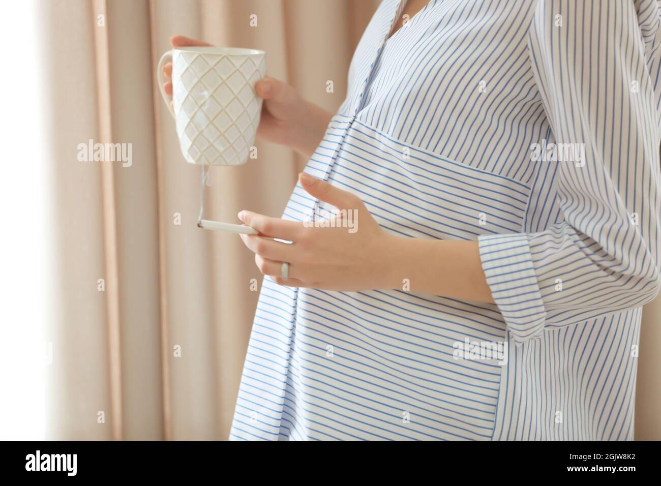 Pregnant woman drinking coffee and smoking cigarette at home Stock
