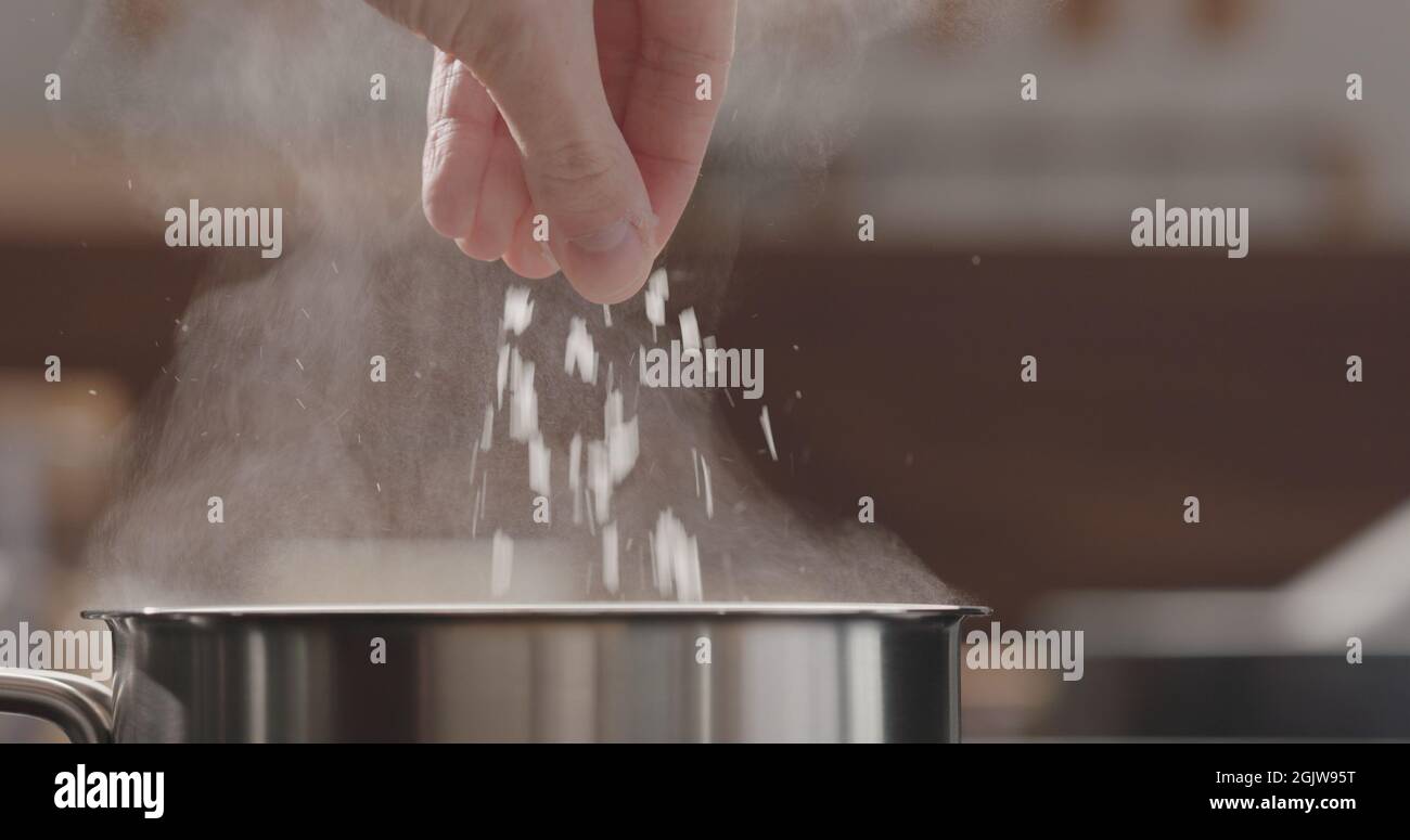 man adding salt to boiling water in saucepan, wide photo Stock Photo