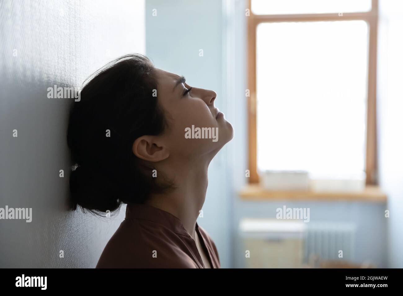 Stressed indian woman with closed eyes sit leaning against wall Stock Photo