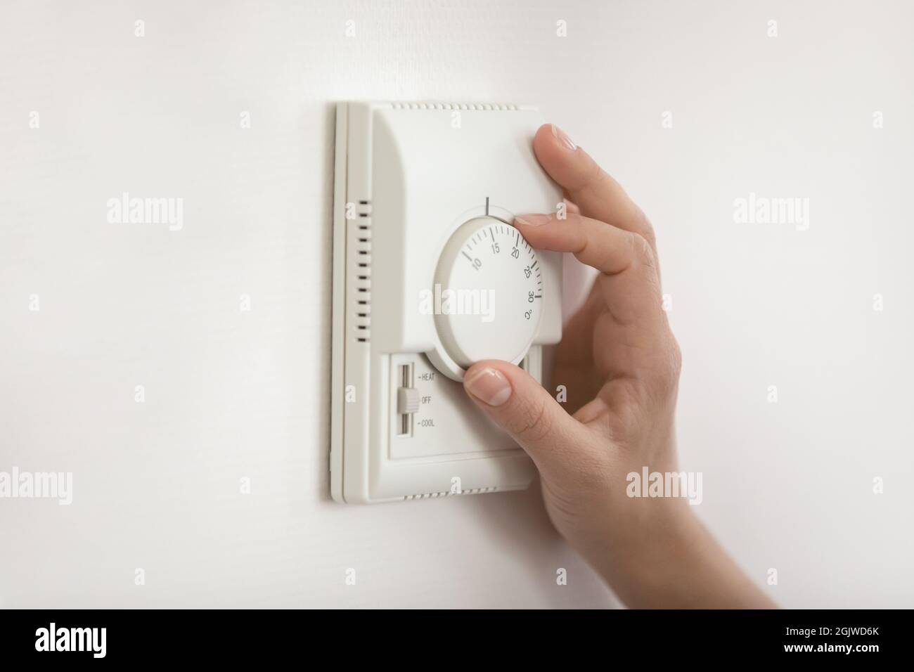 Young woman hand switch on temperature regulator on wall panel Stock Photo